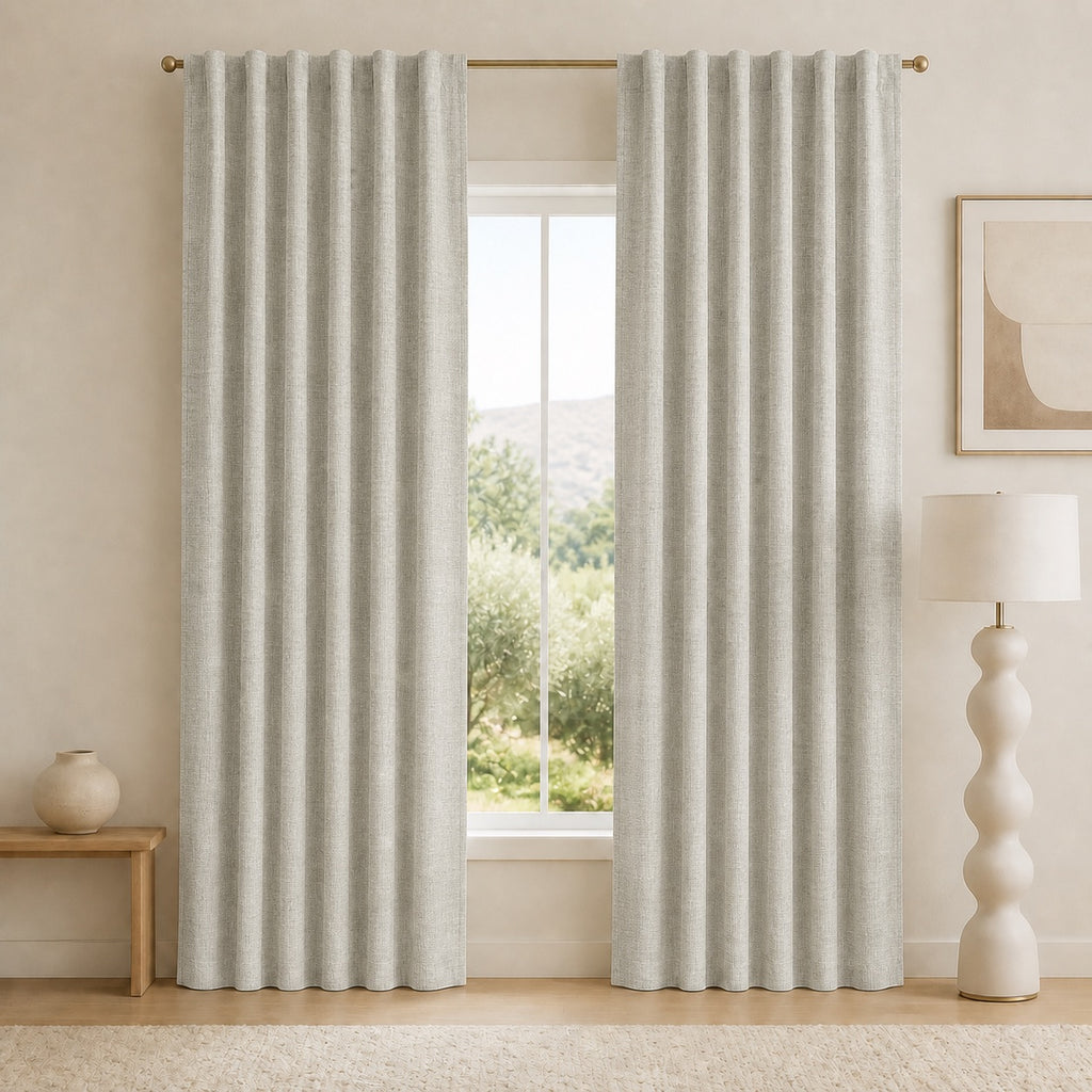 Light gray blackout curtains with vertical pleats and metal grommets, fully hanging beside window.