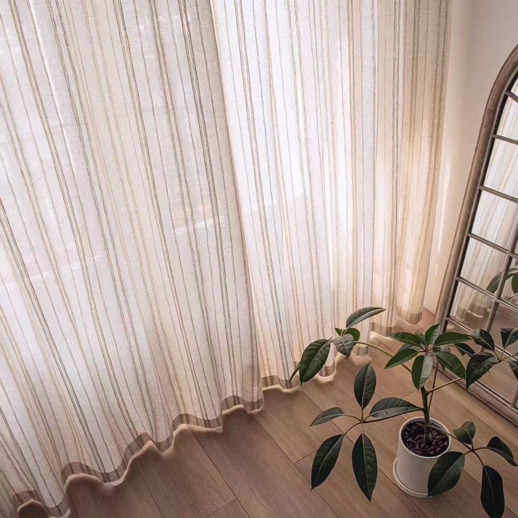 Sheer vertical stripe curtain panel with scalloped hem and draped folds to the floor.