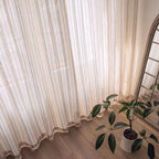 Sheer vertical stripe curtain panel with scalloped hem and draped folds to the floor.