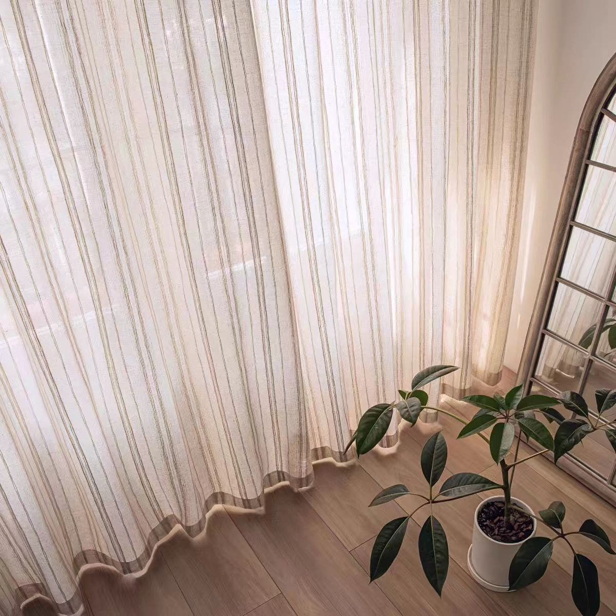 Sheer vertical stripe curtain panel with scalloped hem and draped folds to the floor.