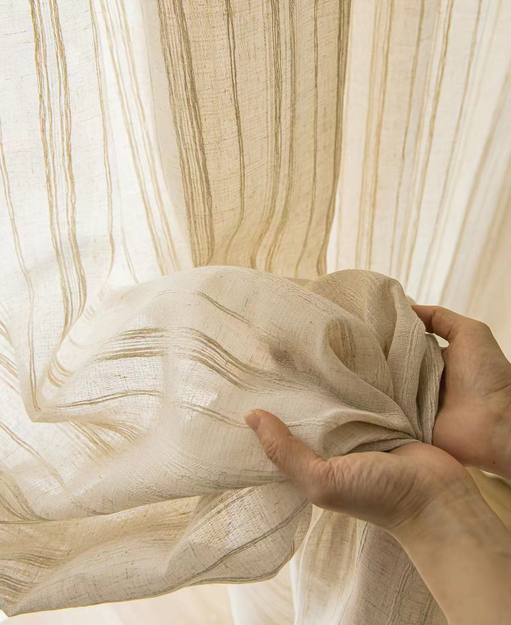 Hands adjusting sheer vertical stripe curtain, showing lightweight linen-blend texture.