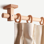 Beech-toned curtain rod with wall bracket and ring finials holding off-white panels