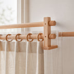 Light wood curtain rod bracket with circular hang rings and beech-toned rod