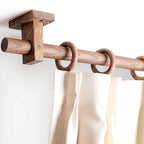 Walnut-toned curtain rod with wall bracket and circular ring finials